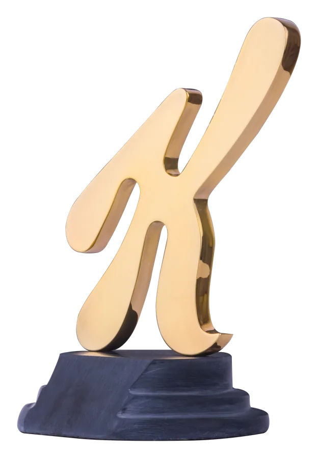 Die Kellogg’s-skrif-K in gepoleerde 24-karaat goud, staande op ’n donker sokkel